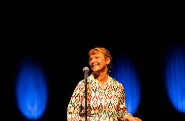 Laura van Dolron glimlacht op podium met microfoon en blauw licht