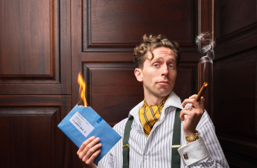 boban benjamin braspenning poseert met blauwe belastingbrieven en een smeulende sigaar. Hij draagt een gestreept overhemd en bretels. 