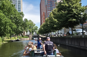 Een boot van de Ooievaart, vaart door de Haagse grachten met op de achtergrond de moderne skyline van Den Haag