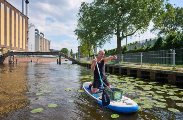 Man op een supboard met een peddel in een kanaal met waterlelies. (c) Phil Nijhuis