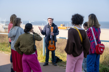 Een muzikant speelt gitaar voor een groep mensen bij het Scheveningse strand.