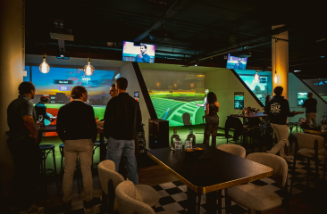 Gruppe von Menschen in einem Indoor-Golfzentrum mit Bildschirmen und Golfspiel.