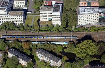 Een trein rijdt langs een groenperk en moderne gebouwen.