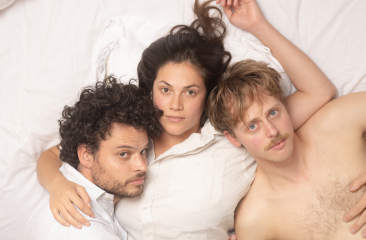 Drie personages liggen op een bed, met gezichten naar de camera. foto: Niels Knelis