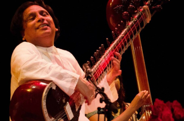 Een muzikant speelt op een sitar met een glimlach.