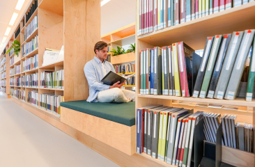 Mann sitzt auf einer Bank in der Bibliothek und liest.