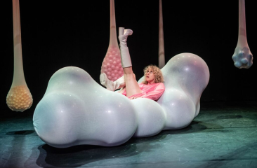 Een persoon in een roze outfit zit op een grote, bolvormige, opblaasbare structuur met kleurrijke elementen.