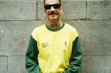 Man met tattoos poseert met een glimlach in de nieuwe collectie van Groen Gele Aderen.