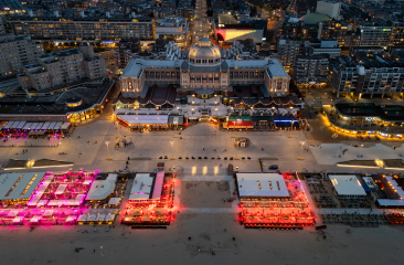 Eine Luftaufnahme von den Strandpavillons in Scheveningen, die nachts beleuchtet sind.