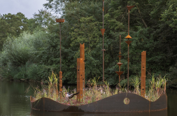 Met gras en bladeren bedekte, metalen sculpturen in het water