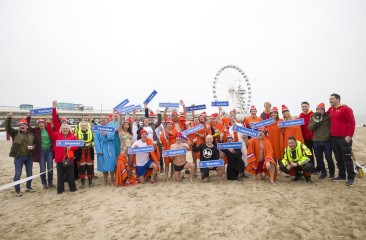 Mensen op het strand van Scheveningen met plaatsnaambordjes die allemaal meedoen aan de Unox Nieuwjaarsduik 2026.