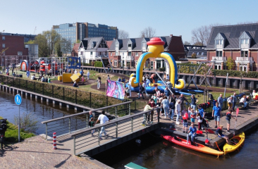 Mensen genieten van een zonnige dag bij een speelplaats met wateractiviteiten en tenten in Den Haag.