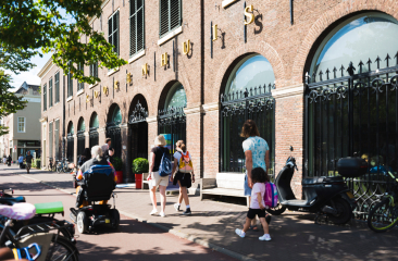 Voorkant van het Koorenhuis op een zonnige dag waar mensen langs lopen en rijden in een scootmobiel