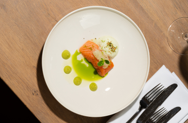 Ein Teller mit Lachs, weißer Sauce und grünen Tropfen.