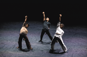 Three dancers performing a choreography on stage.