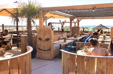 Een zonnige strandbar met houten meubels en palmbomen.