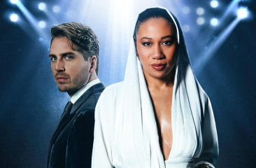 Twee acteurs staan in het licht, een man in een zwart pak en een vrouw in een witte jurk.