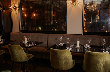 Gedeckte Tische bei Kerzenschein, Samtstühle und Spiegelwände in einem stimmungsvollen Restaurantinterieur