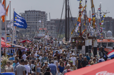 Vlaggetjesdag Scheveningen met een haven vol zomers geklede mensen en boten versierd met vlaggetjes. 