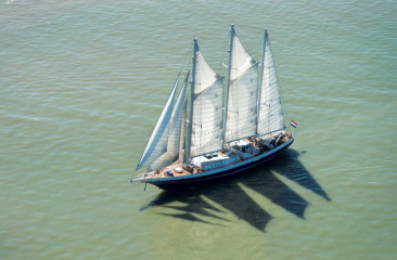 A sailing ship with white sails is sailing on calm water.