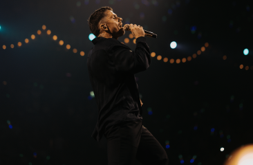 Een zanger staat in de spotlight en zingt met een microfoon.