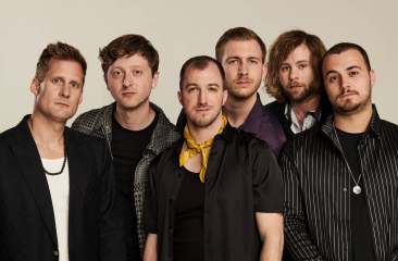 Zes mannen poseren samen met verschillende kleurrijke outfits.