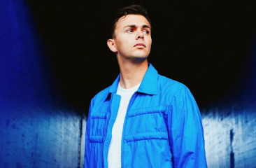 Jongeman staat in een blauwe gang met een neutrale uitdrukking.