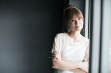 Vrouw met een lichte blouse leunt tegen het raam.