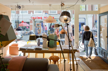 Een blik op een winkelinterieur met lampen en mensen buiten.
