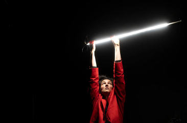 A person in a red outfit holds a light bar above their head.