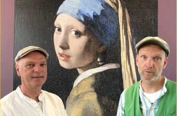 Twee mannen met pet poseren voor een groot kunstwerk van Vermeers Meisje met de parel