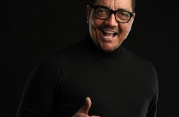 Man in zwarte trui glimlacht en geeft een duim omhoog.