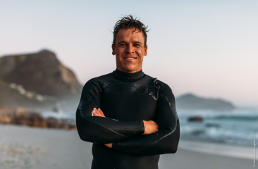 Man in wetsuit met een glimlach op het strand