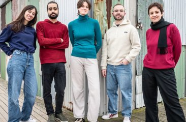 Five members of Sketch351 standing on a wooden floor, in front of a metal background, in The Hague.