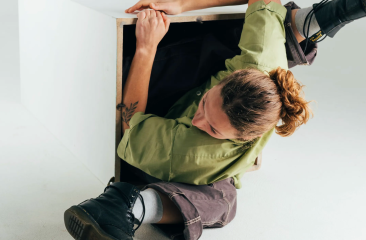 A person wearing a green shirt climbing into a box.