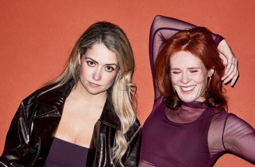 Twee vrouwen poseren samen met een oranje muur op de achtergrond.