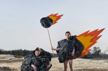 Twee personen verkleed als vurige meteorieten in zanderig duinlandschap met blauwe lucht