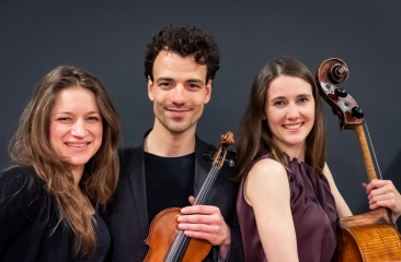 Drie musici poseren met viool en cello tegen een donkere achtergrond