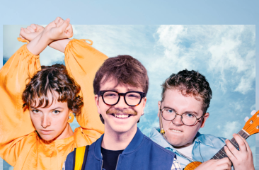 Drie jonge artiesten poseren speels voor een heldere lucht met wolken. Links een vrouw in een oranje blouse met opgestoken armen, in het midden een man met een grote glimlach en bril, rechts een man met bril en een ukelele.