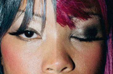 Close-up van gezicht met contrasterende make-up en haarkleuren; ene oog open, andere dicht