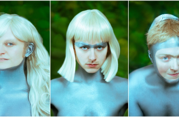 Drieluik van drie personen met metallic zilver geschminkte huid, futuristische pruiken en accessoires, poserend tegen een groene achtergrond.