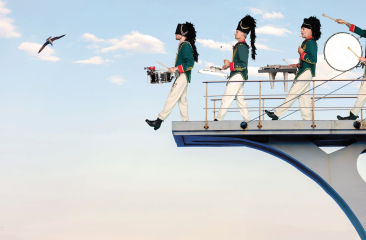 De leden van percossa lopen in hun uniform met hun instrumenten een duikplank af. 