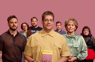 Groep van zeven mensen poseert voor een roze achtergrond; de man in het midden houdt een boek vast.