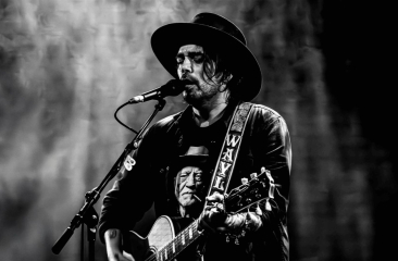 Zanger Waylon met gitaar en hoed zingt in microfoon tijdens liveoptreden