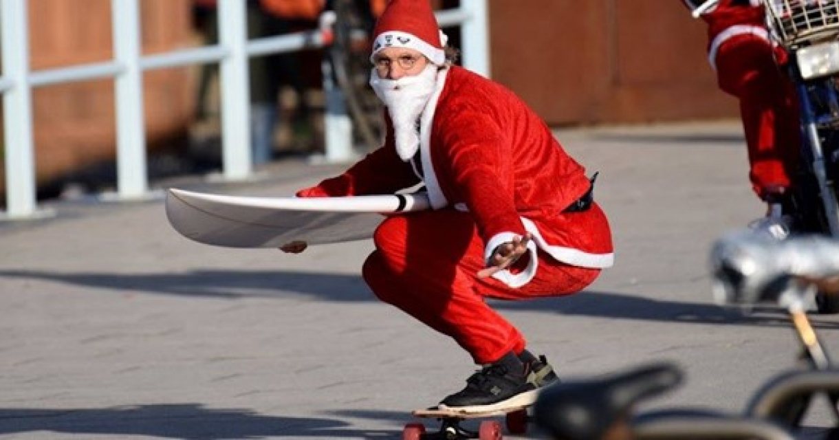 Surfdude in kerstman outfit op skateboard met surfplank Surfdude in kerstman outfit op skateboard met surfplank