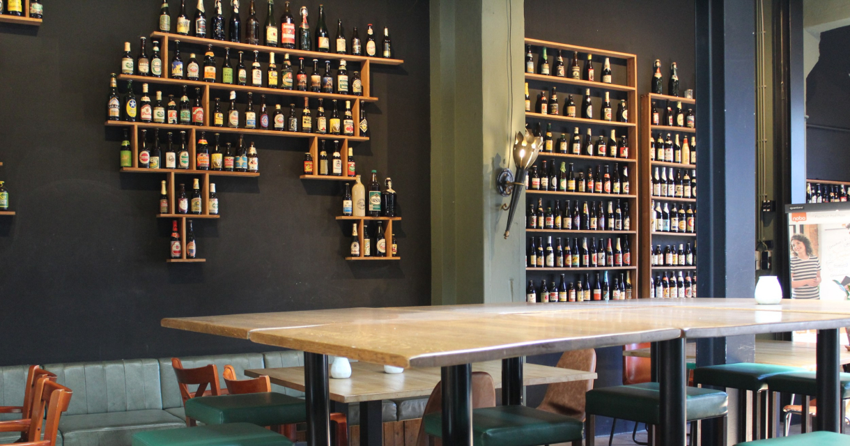 Biertafels bij Brouwerij De Prael met aan de muur een rek met verschillende biertjes.