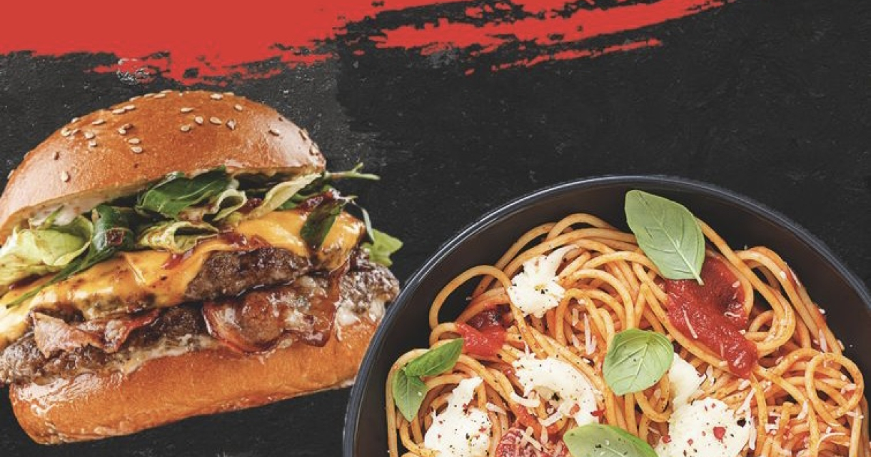 Een goed gevuld broodje cheeseburger en een bordje spaghetti met tomatensaus en baslicumblaadjes Een goed gevuld broodje cheeseburger en een bordje spaghetti met tomatensaus en baslicumblaadjes