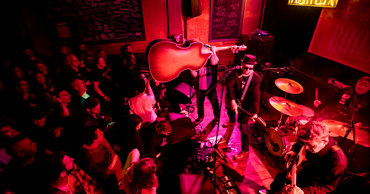 Foto van boven van publiek en een band op het podium van de Zwarte Ruiter. De bassist tilt de bas hoog op