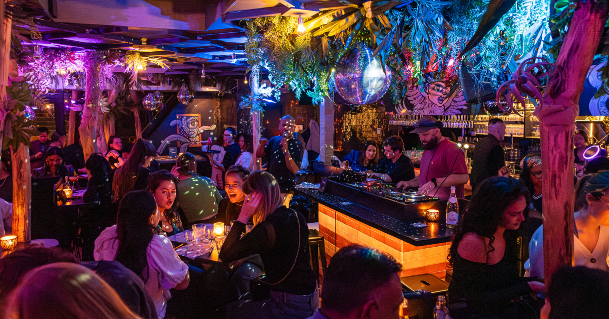 De foto toont een levendige en sfeervolle bar met een tropisch en modern interieur. 