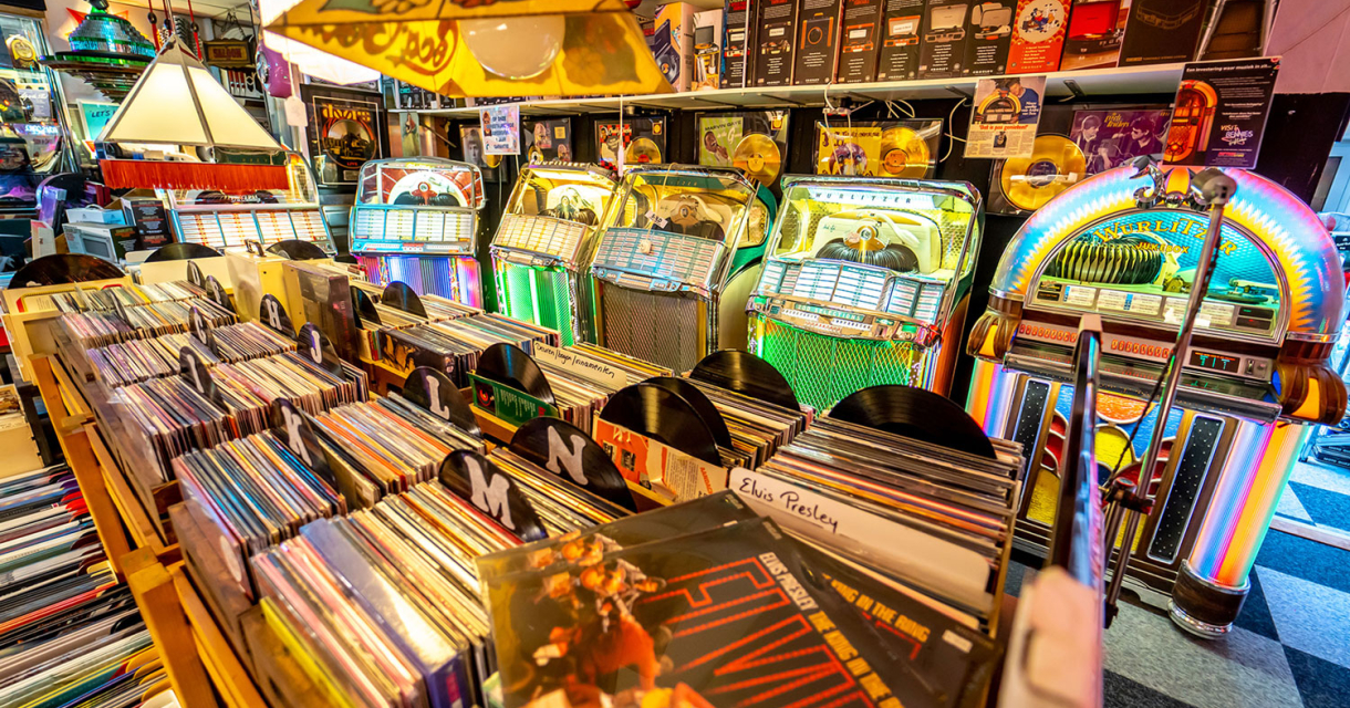 Retro muziek- en platenwinkel met vinylbakken, kleurrijke jukeboxen en vintage muziek, waaronder Elvis Presley-platen en gouden records.